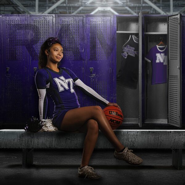 Young female cheerleader sitting on a locker room bench with her hand on a basketball