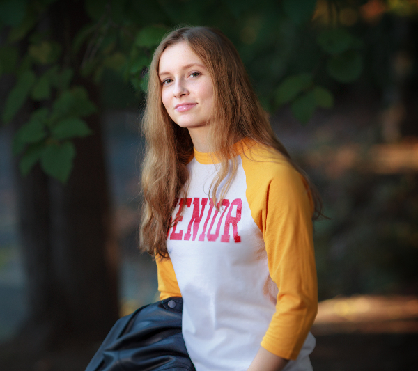 A high school senior with a shirt that says SENIOR and she's in front of a tree background to illustrate senior photography