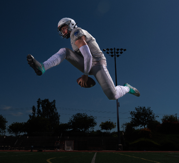 A football player jumping high in the air holding the football between his legs to illustrate senior photography